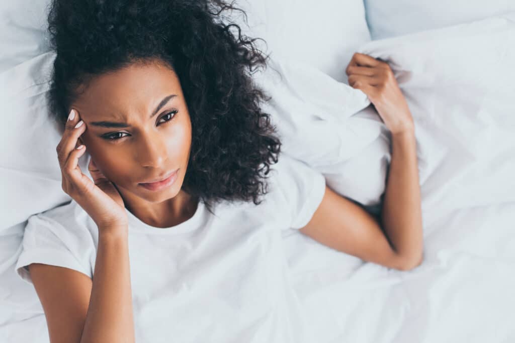upset african american woman suffering from headache while lying in bed