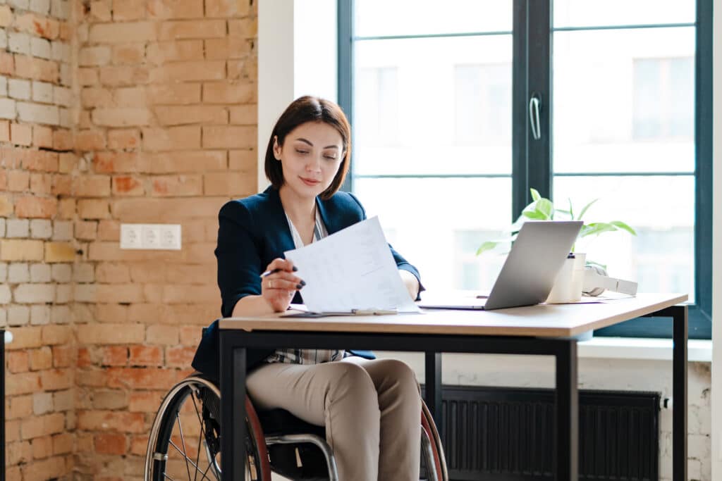 White young woman in wheelchair working with papers and laptop in office
