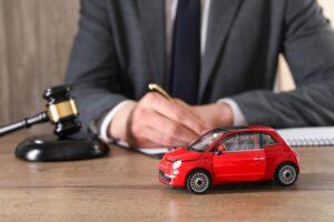 A lawyer, sitting at a desk with a wooden car and a gavel on the desktop, prepares to explain what the average car accident settlement is worth.